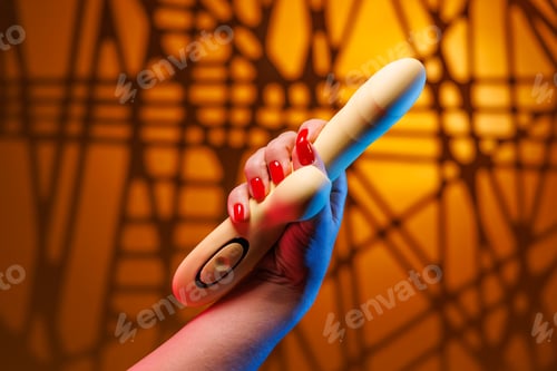 Preview: A soft female hand with a striking red manicure firmly holds a yellow vibrator for intimate play.