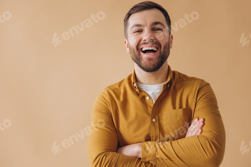 Preview: Portrait of a modern millennial bearded man happy and smiling in a yellow shirt on beige background