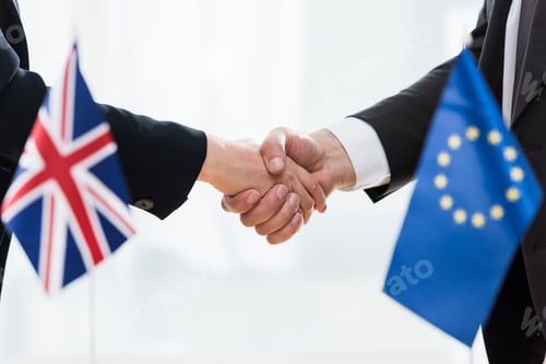 Preview: cropped view of diplomats shaking hands near european union and united kingdom flags