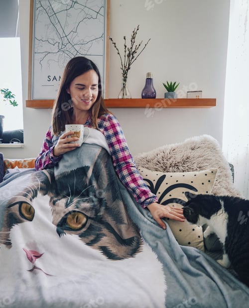 Preview: Smiling young woman bundled up in a blanket on a couch.