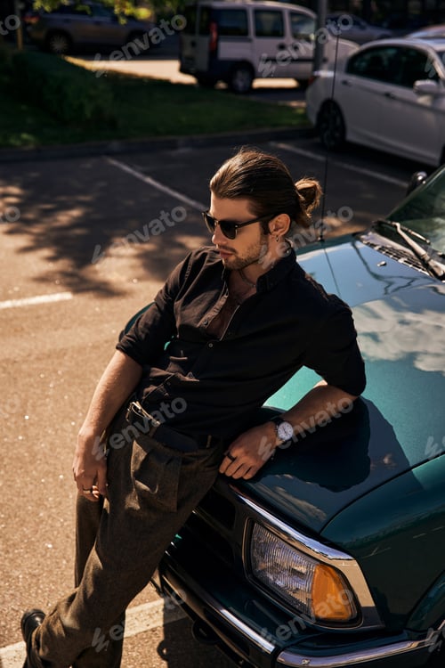 Preview: stylish appealing man with sunglasses in black outfit leaning on car and looking away, sexy driver