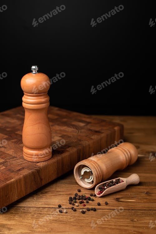 Preview: Pepper mill and whole pepper in wooden scoop on black table.