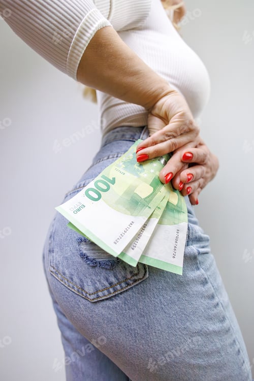 Preview: The girl holds hundred euro bills near her hip. A girl in jeans with a euro banknote in her hands.