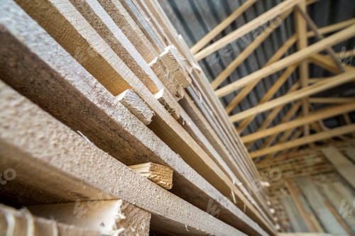Preview: Neatly piled long stack of wooden boards inside attic room under construction.