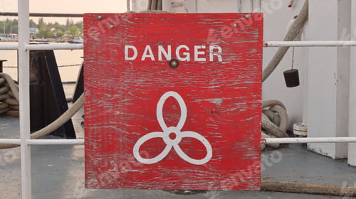 Preview: A Red Danger sign with White Font depicting a boat propeller symbol. Wooden. Attached to railing.