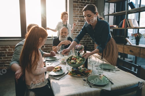 Preview: smiling woman serving salad on plate during family dinner at home