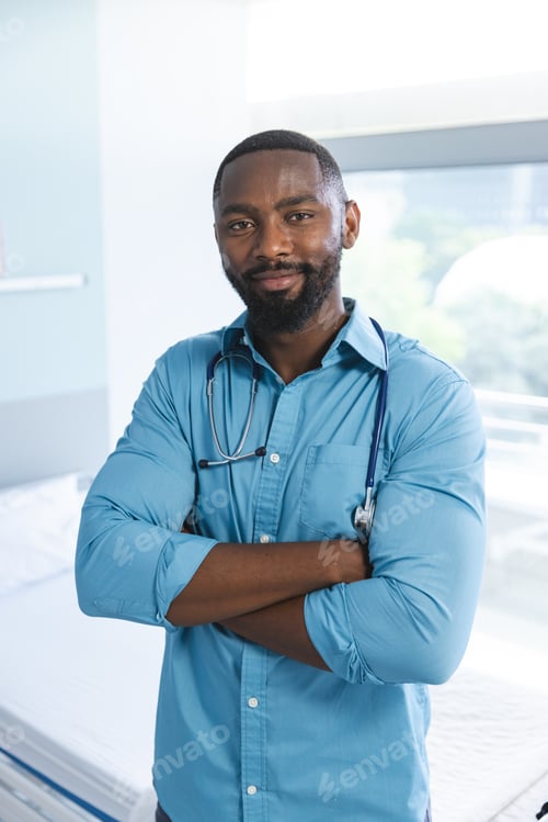 Preview: Portrait of happy african american male doctor wearing blue shirt and stethoscope in hospital room
