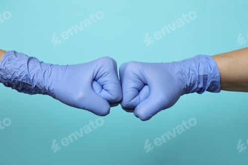 Preview: Hands in medical gloves greeting with fist bump on blue background