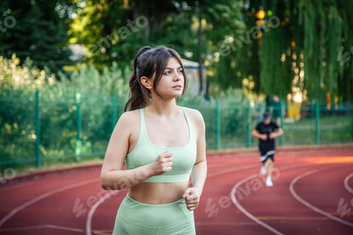 Preview: Attractive young woman in sportswear jogging at the stadium.