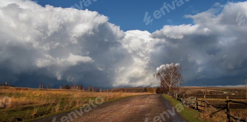 Preview: Vast sky filled with dramatic clouds above a country road during a clear day in autumn