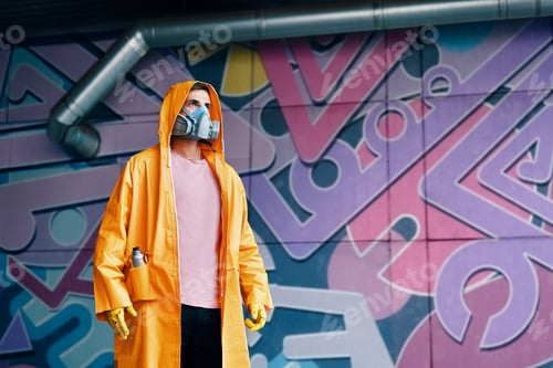 Preview: Graffiti painter in respirator mask standing near the wall with his paintings