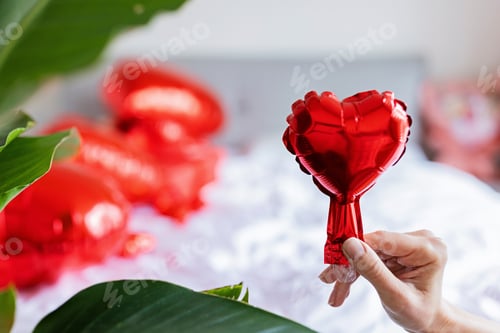 Preview: woman hand holding red foil heart at home