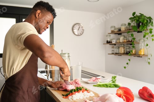 Preview: Young black man de-boning chicken to prepare a recipe.