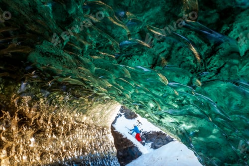 Preview: View through glacial ice cave with climber in the background.