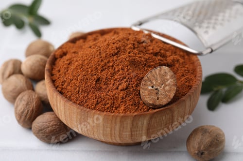 Preview: Nutmeg powder in bowl and seeds on white table, closeup