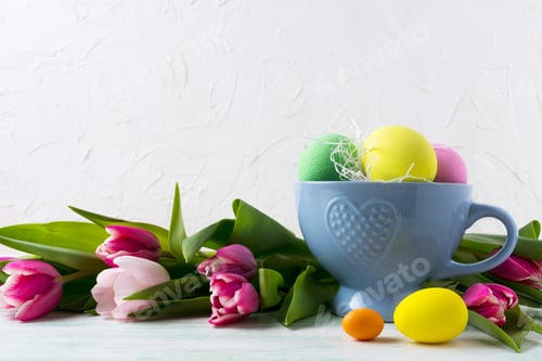 Preview: Easter hand painted eggs in blue cup and pink tulips background