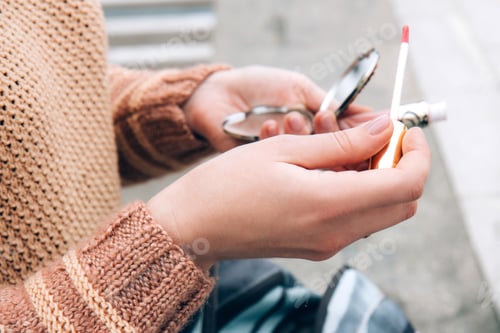 Preview: A young woman holds a mirror and lip gloss in her hands. Woman applying makeup
