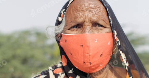 Preview: Closeup of an elderly Indian female wearing a vibrant orange Coronavirus mask on a blurry background