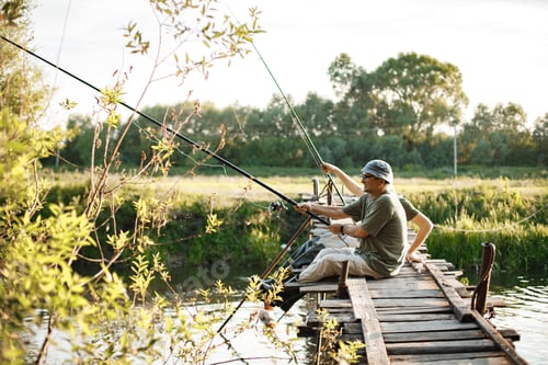 Preview: Two fishermen with fishing rods on a footbridge near the lake at summer