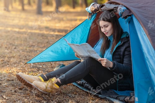 Preview: Young woman checking map in camping tent