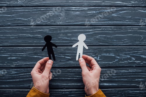 Preview: Top view of man holding black and white human figures on dark wooden background