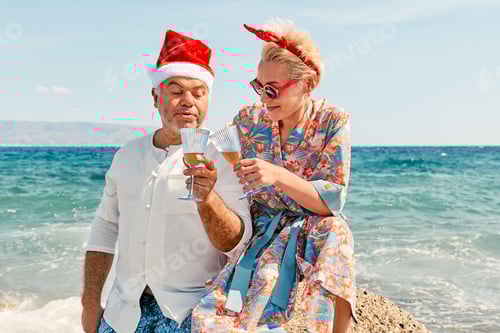 Preview: Funny couple in christmas costumes drinking wine and enjoying christmas vacations on tropical beach