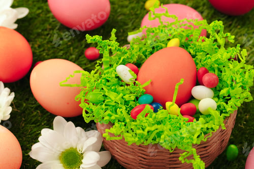 Preview: Close up photo of colored Easter eggs and candies on grass