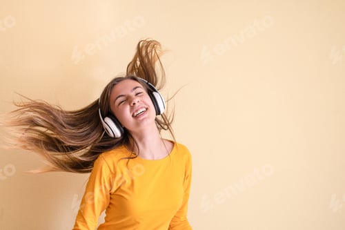 Preview: Young girl with headphones having fun on yellow wall background