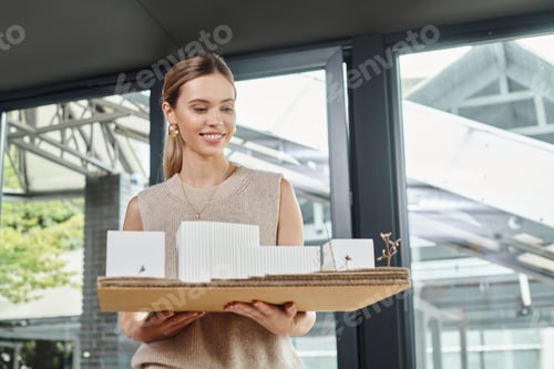 Preview: cheerful employee in smart pastel attire looking at scale model of building, design bureau