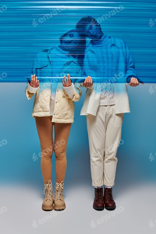 Preview: interracial couple in leather boots holding blue plastic sheet in studio, winter fashion concept