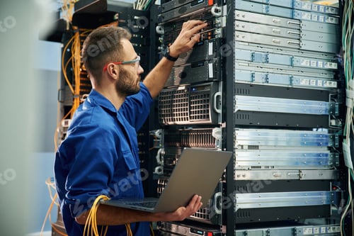 Preview: Using the laptop. Young man is working with internet equipment and wires in server room