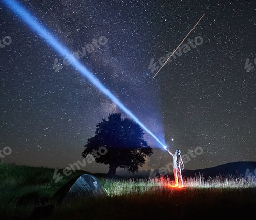 Preview: Spaceman directs a ray of light into the sky with a help of a lantern in the night in the mountains