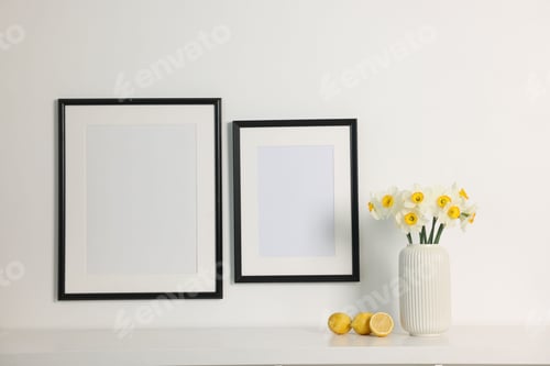 Preview: Beautiful daffodils in vase on white table and picture frames indoors