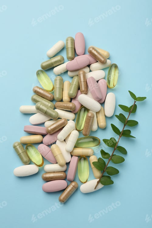 Preview: Different vitamin pills and green branch on light blue background, flat lay