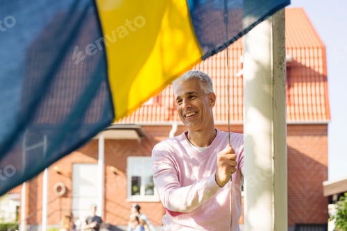 Preview: Man smiling as he raises a colorful flag on a sunny day