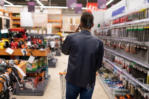 Preview: a buyer in a hardware store talking on the phone while walking between the rows of machinery