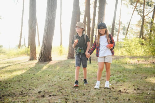 Preview: boy and girl go hiking with backpacks on forest road bright sunny day