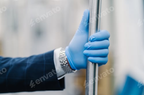 Preview: Mans hand in blue disposable glove touching handrail in public transport