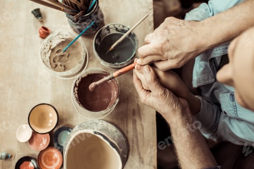 Preview: Overhead view of girl painting clay pot and grandparents helping at workshop
