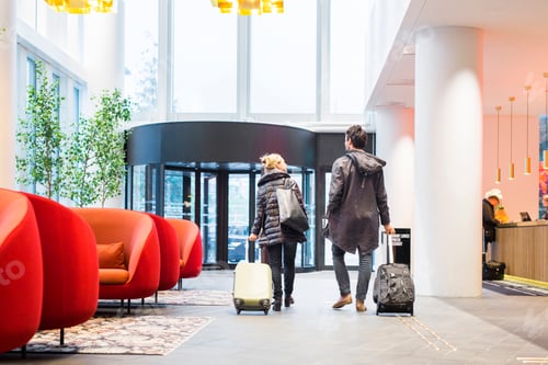 Preview: Rear view of business people with luggage walking at hotel lobby