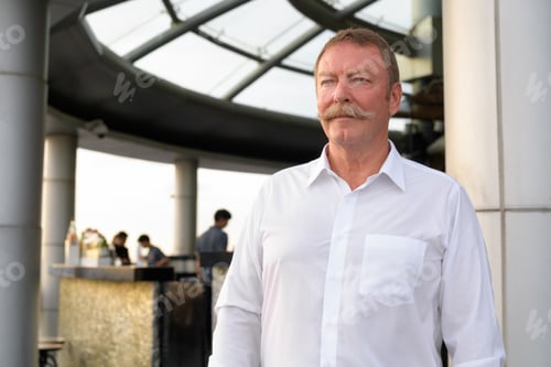 Preview: Handsome senior businessman thinking while looking away at the rooftop restaurant