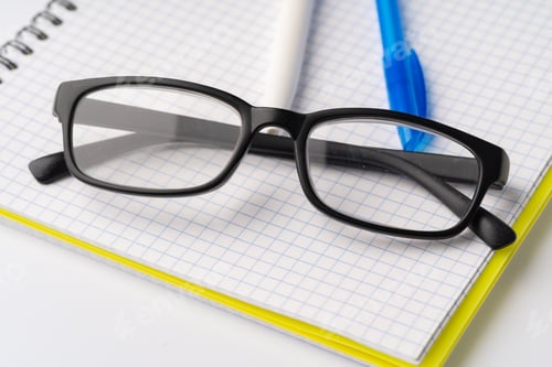 Preview: Two pens and glasses on open notepad, close up