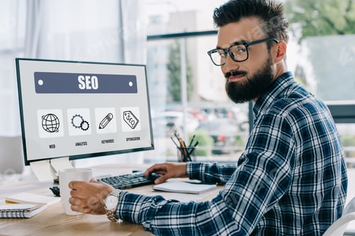 Preview: young successful seo manager sitting at workplace with computer and looking at camera