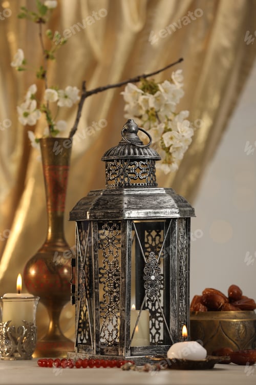 Preview: Arabic lantern, misbaha, candles, dates and flowers on table against blurred lights