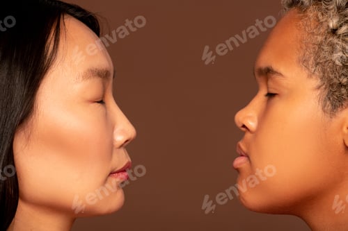 Preview: Side view of faces of two young intercultural women standing in front of camera