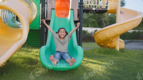 Preview: A young girl is sitting on a green slide in a park