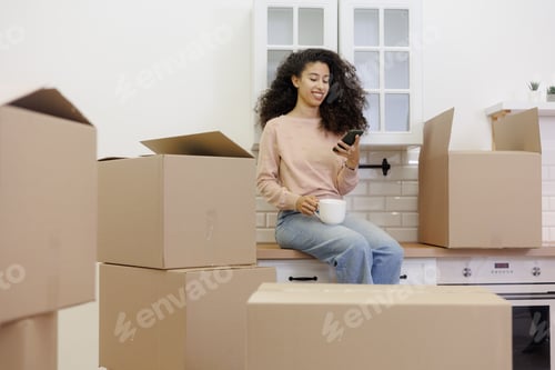 Preview: Woman Smiles With Smartphone, Moving Boxes In Kitchen