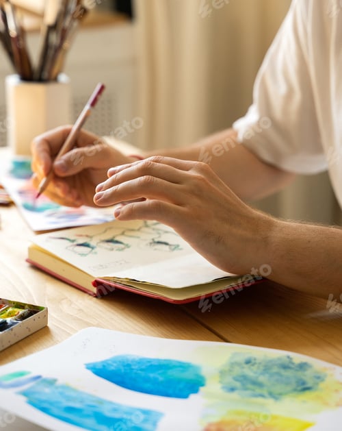 Preview: The artist's hands with a brush. An artist's sketchbook lying on the desktop. The workflow of creati