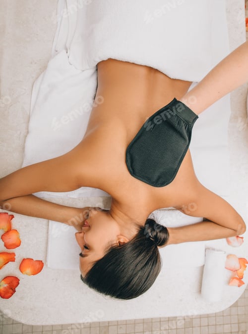 Preview: Mixed race woman heaving skin peeling in hammam. Peeling with a glove KESE is performed in the
