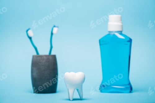 Preview: Model of tooth near toothbrushes and mouthwash on blurred background on blue background